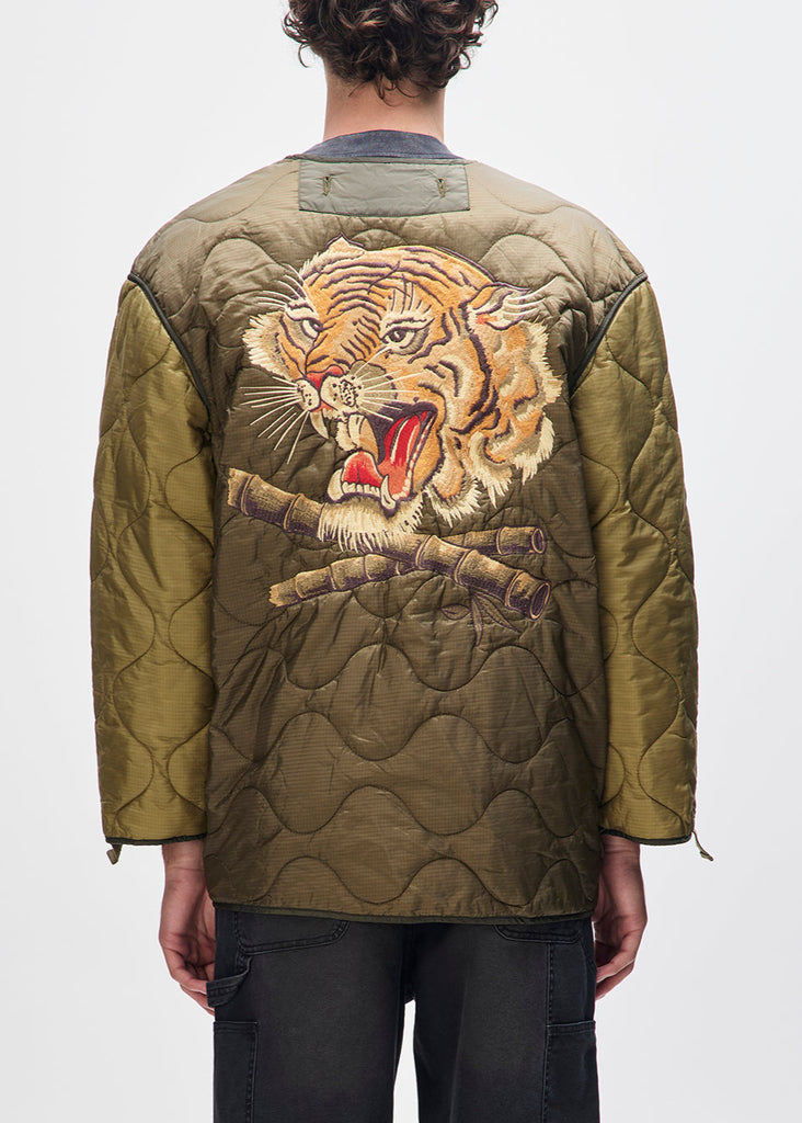 Person wearing a green quilted jacket with a tiger design on the back against a white background