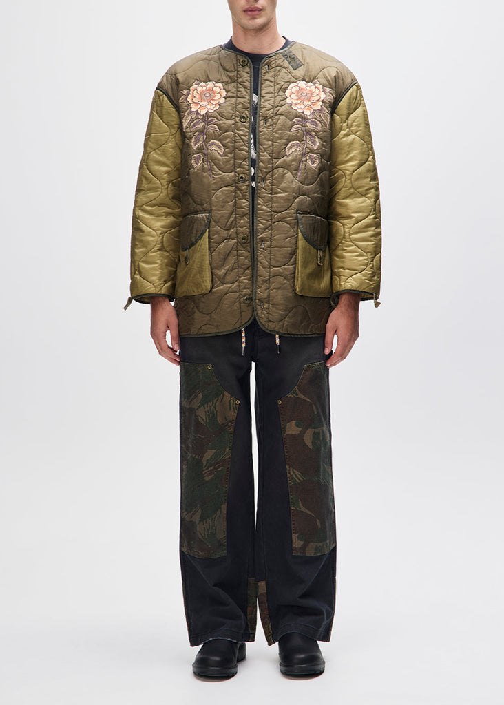 Person wearing a green quilted jacket with floral embroidery on a white background