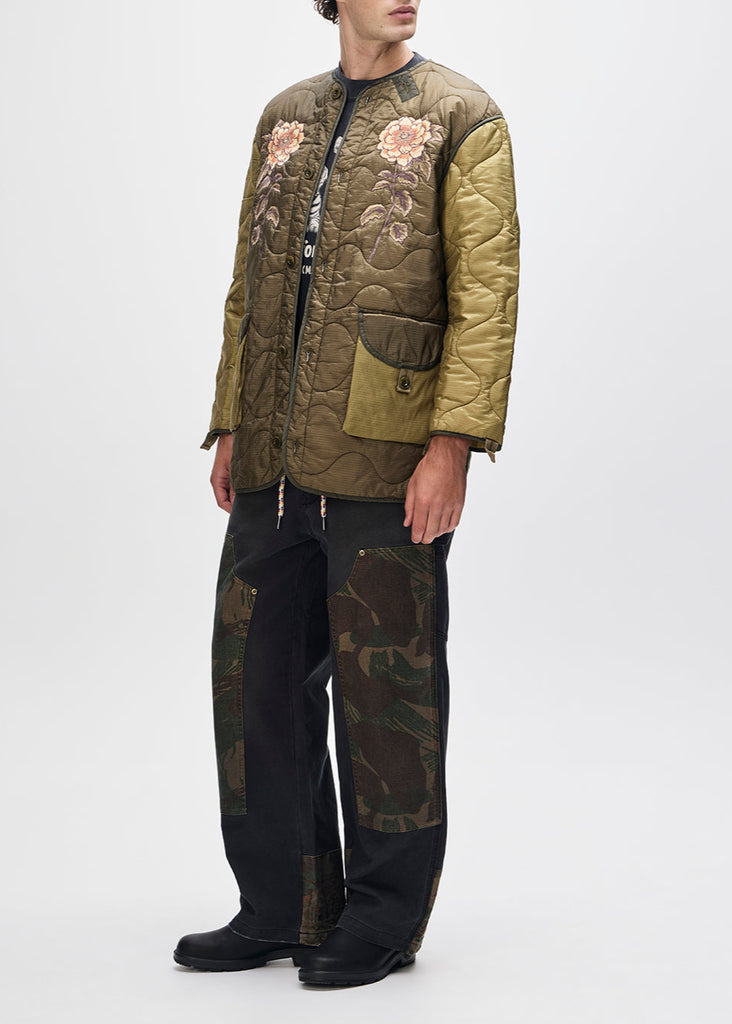 Person wearing a green quilted jacket with floral embroidery and camouflage pants on a white background
