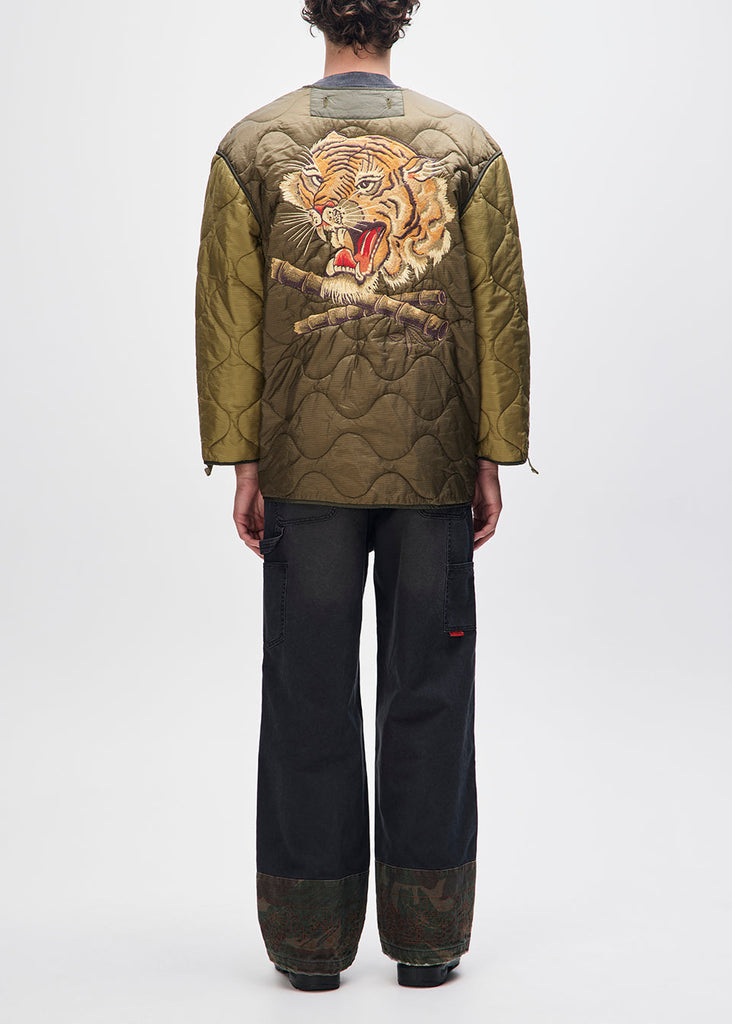 Person wearing a green quilted jacket with a tiger design on a white background