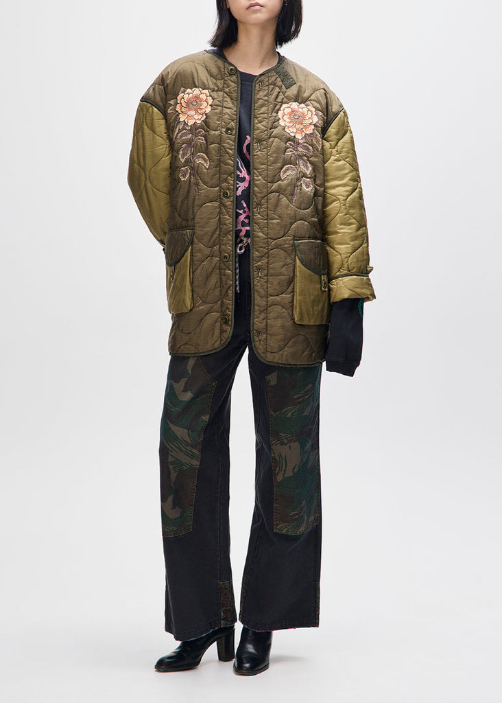 Person wearing a green quilted jacket with floral embroidery on a white background