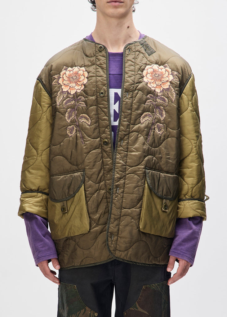 Person wearing a green quilted jacket with floral embroidery on a white background
