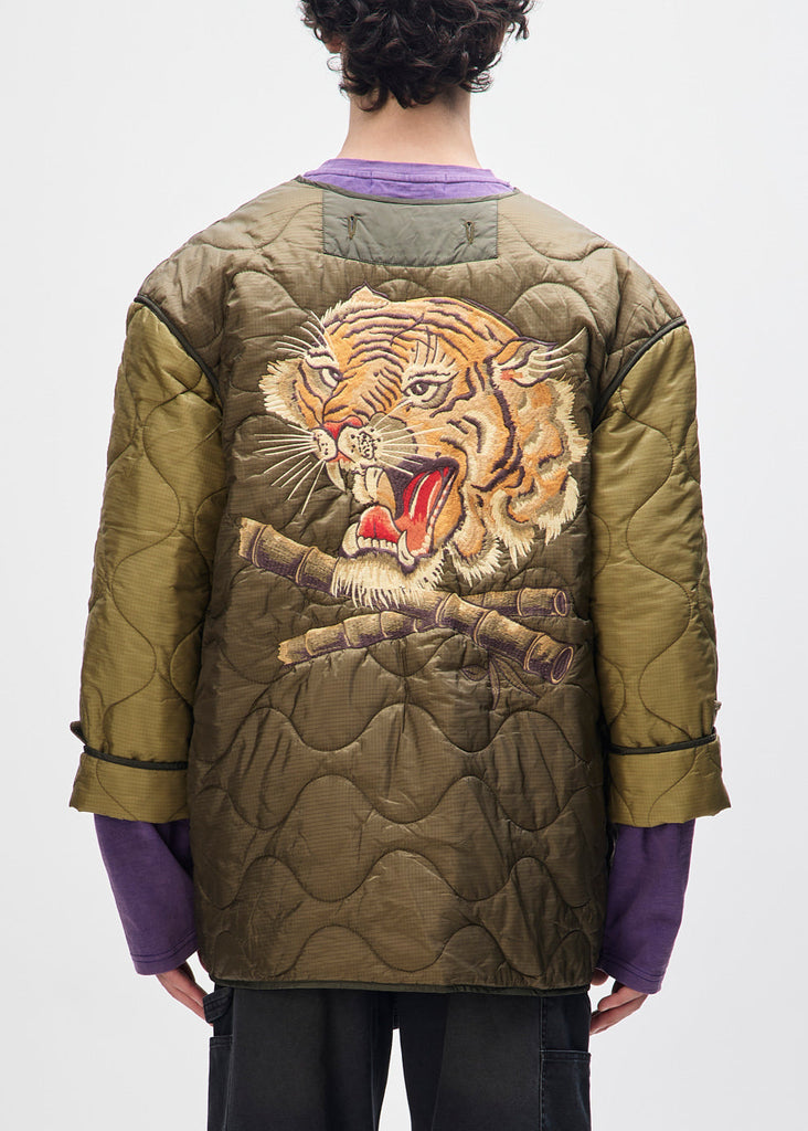 Person wearing a green quilted jacket with a tiger design on a white background