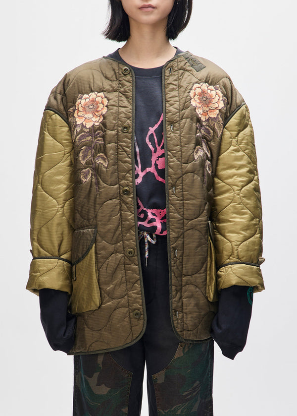 Person wearing a green quilted jacket with floral embroidery on a white background