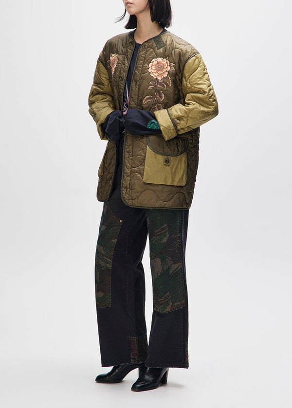 Person wearing a green quilted jacket with floral embroidery on a white background