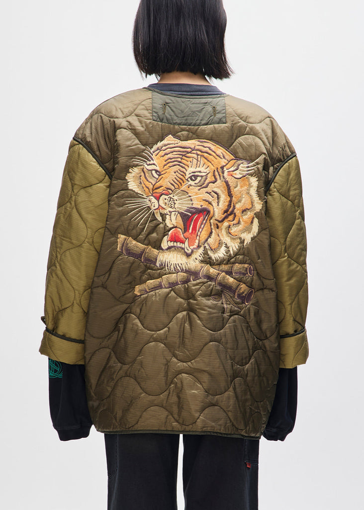 Person wearing a quilted jacket with a tiger design on the back against a white background