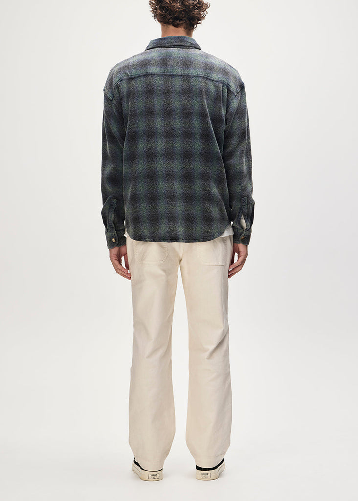 Person wearing a dark plaid shirt and light-colored pants on a white background