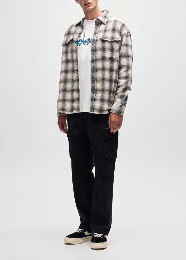 Person wearing a plaid shirt over a graphic t-shirt with black pants on a white background