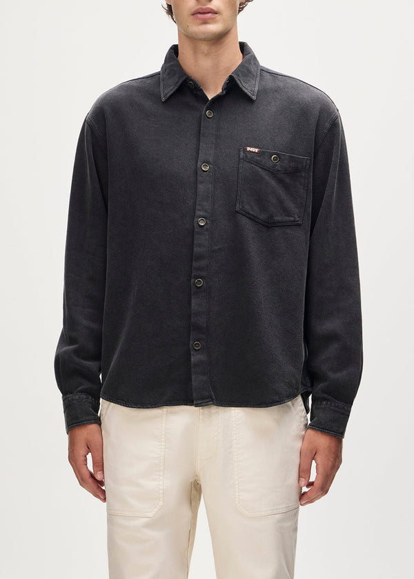 Person wearing a dark gray button-up shirt with a pocket on a light gray background