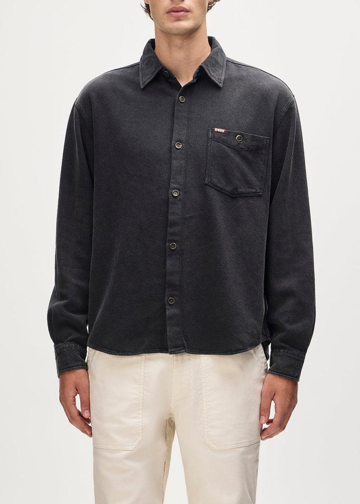 Person wearing a dark gray button-up shirt with a pocket on a light gray background