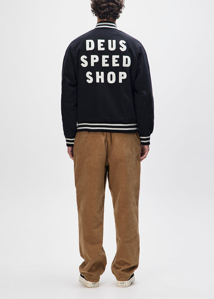 Person wearing a black jacket with 'Deus Speed Shop' text on the back, standing against a white background.
