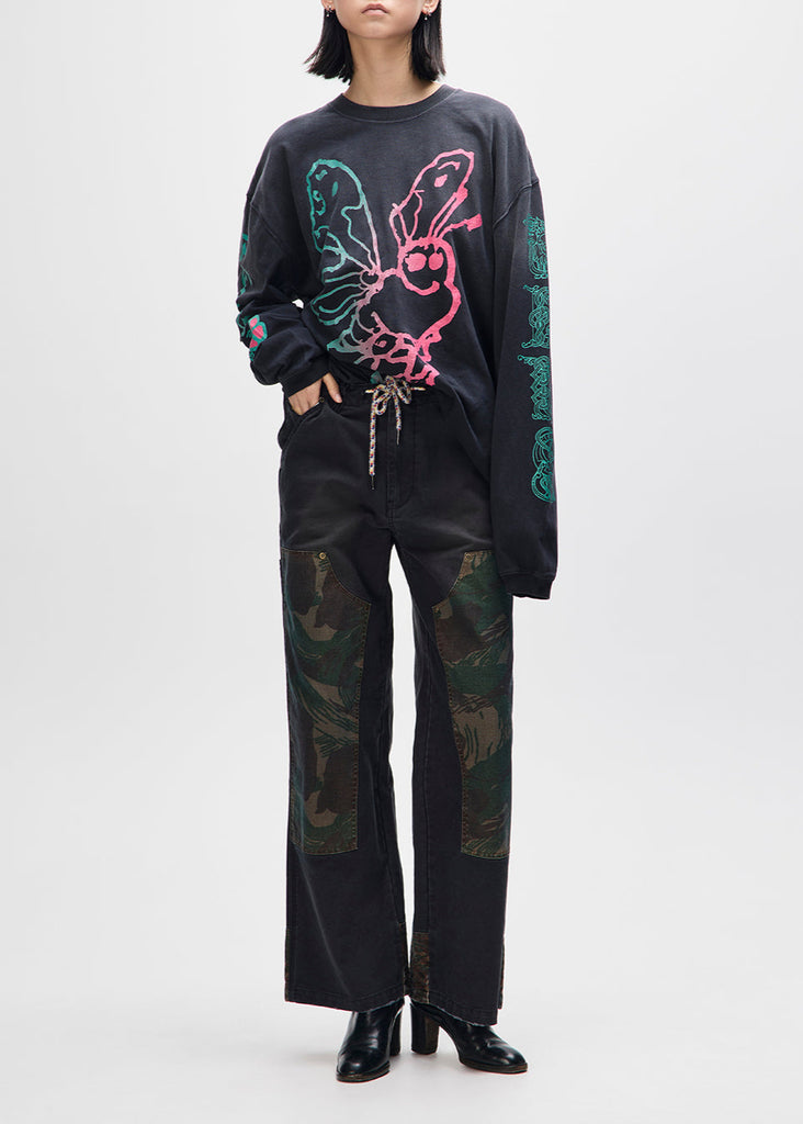 Person wearing a black sweater with colorful butterfly design and black pants with camouflage pattern on a white background
