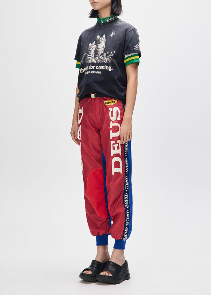 Person wearing a black t-shirt with graphic design and red 'DEUS' pants on a white background