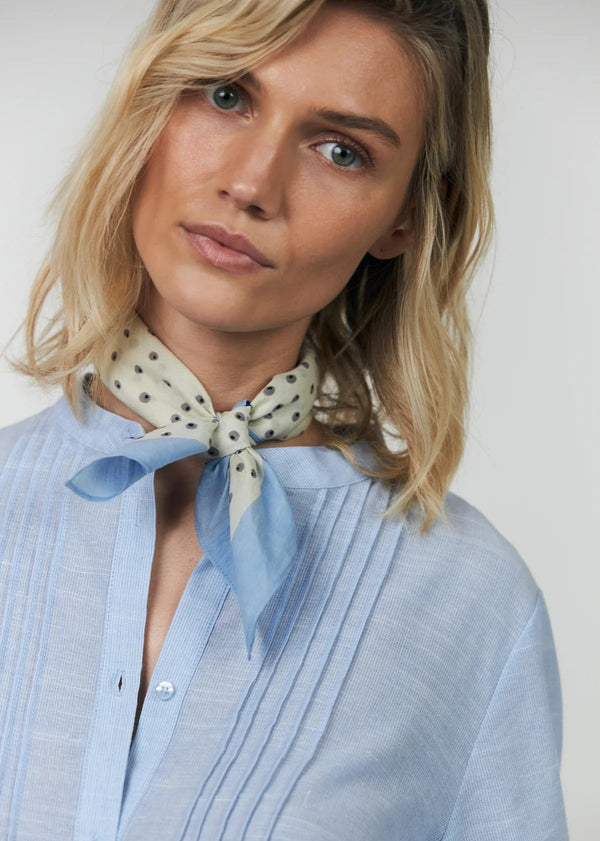 Woman wearing a light blue shirt and a patterned scarf with a plain background