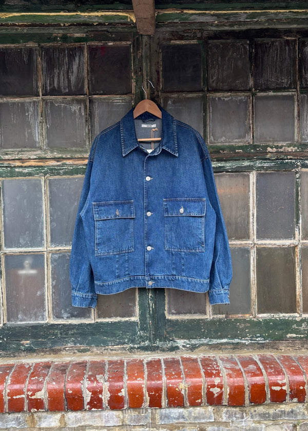 Blue denim jacket hanging on a brick wall with a rusty metal roof above.