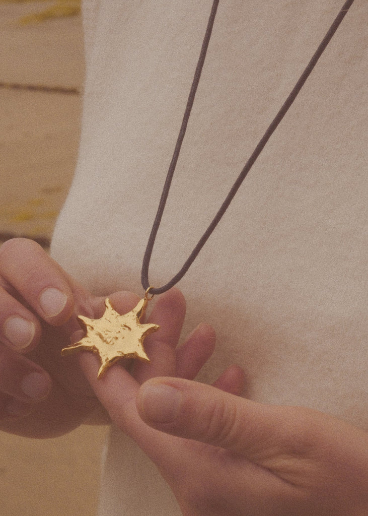 Gold star-shaped pendant on a dark cord held by a person against a neutral background