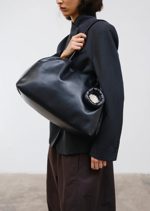 Person holding a large black leather bag against a plain background