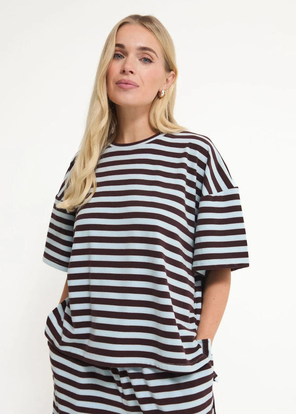 A woman modeling an oversized short-sleeve top with horizontal dark brown and light blue-gray stripes, paired with matching striped bottoms, against a plain white studio background.