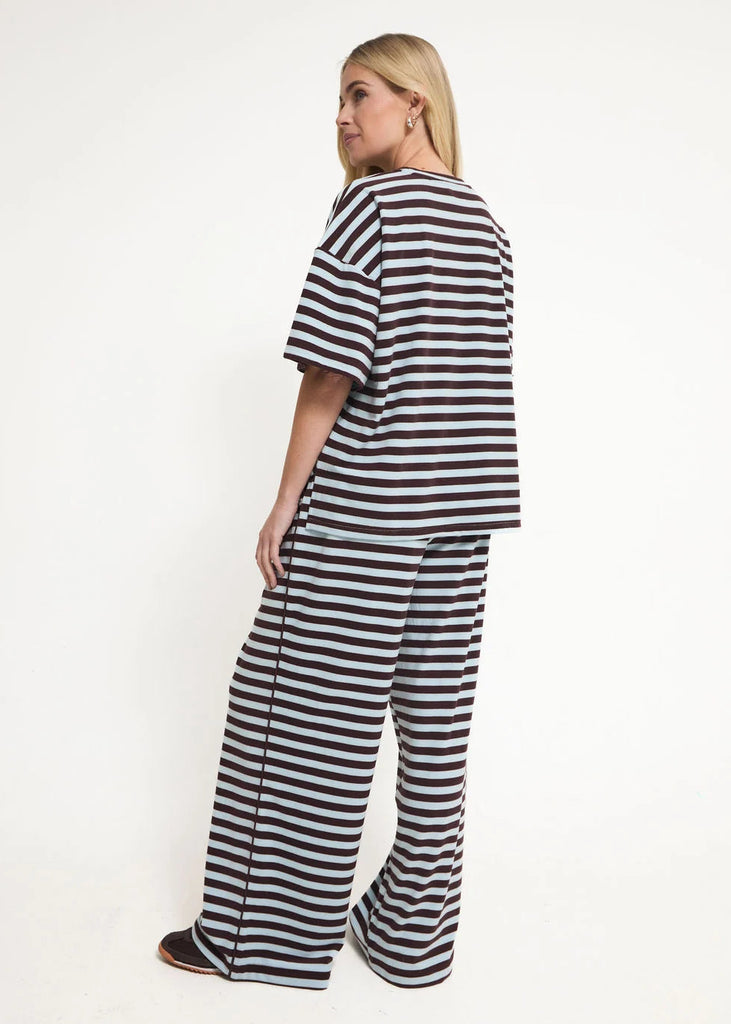 A woman modeling a matching two-piece loungewear set with black and white horizontal stripes, shown from a side-back angle against a plain white studio background.