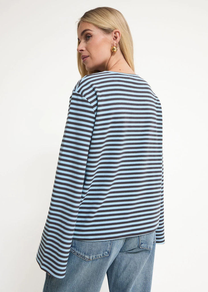 A woman shown from the back wearing a loose, long-sleeve striped top with navy, gray, and white horizontal stripes, paired with blue jeans, against a plain white studio background.