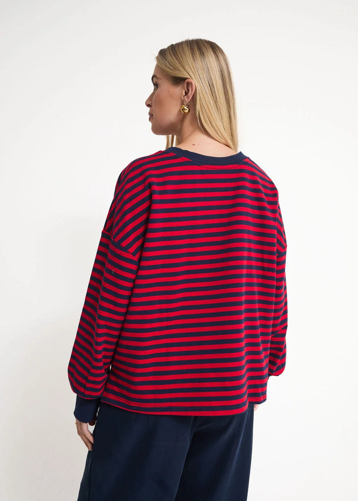 A woman shown from the back wearing a red and navy blue horizontally striped long-sleeve top and navy pants, photographed against a plain white studio background.