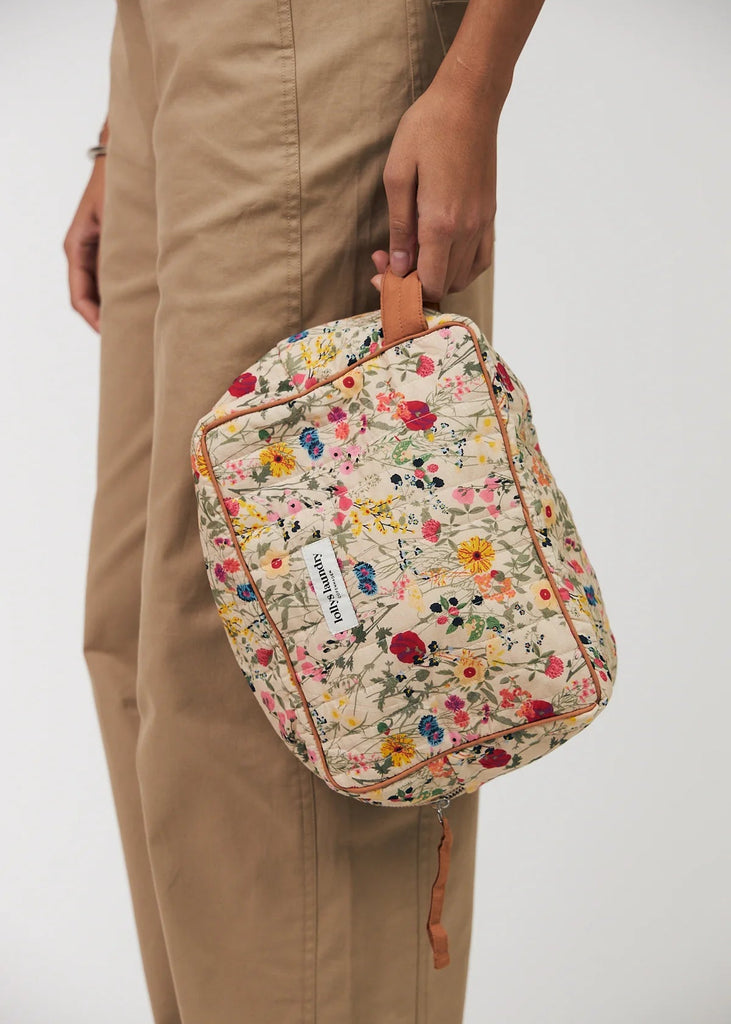 Floral-patterned bag held by a person wearing beige pants on a plain background