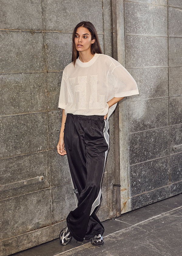Woman wearing a white top and black pants with a stripe, standing against a gray stone wall.