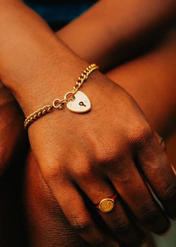 Close-up of a hand wearing a gold bracelet and ring with a heart charm.