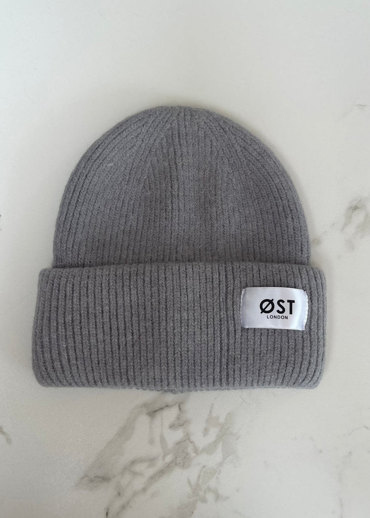 Gray knit beanie with a white label on a light marble background