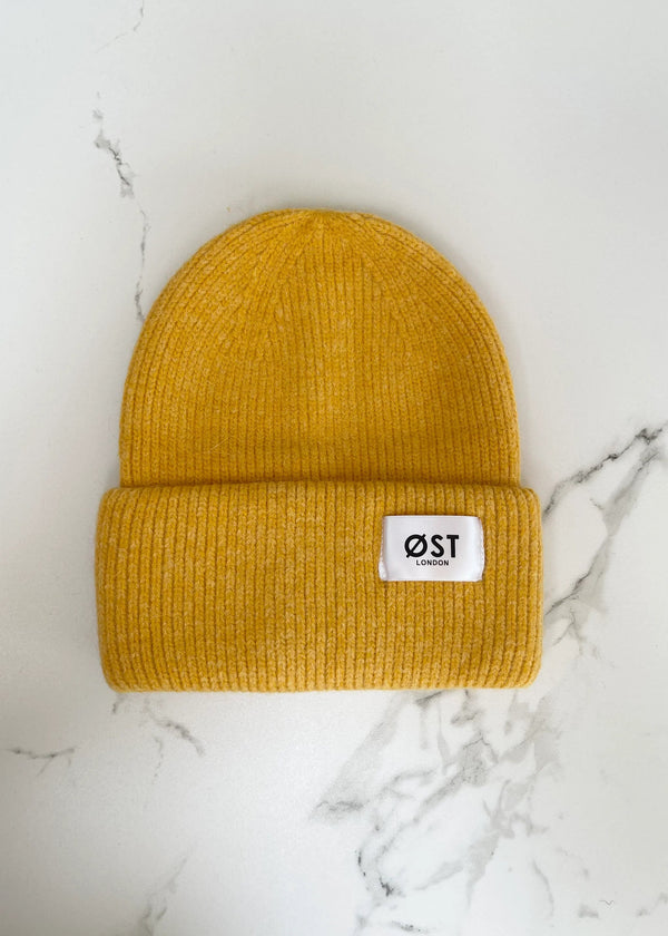 Mustard yellow beanie with a white label on a marble background