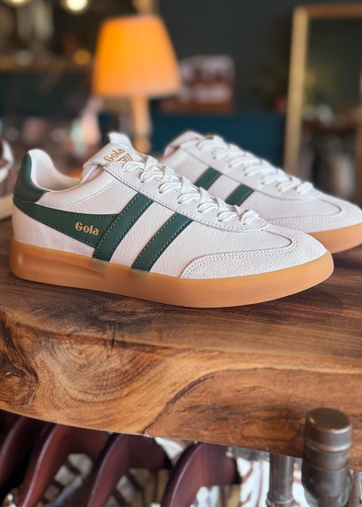 Pair of white sneakers with green accents on a wooden table.