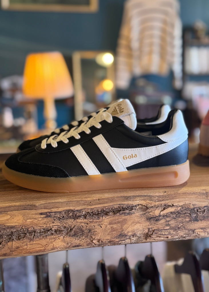 Black and white sneakers with 'Gola' branding on a wooden surface.