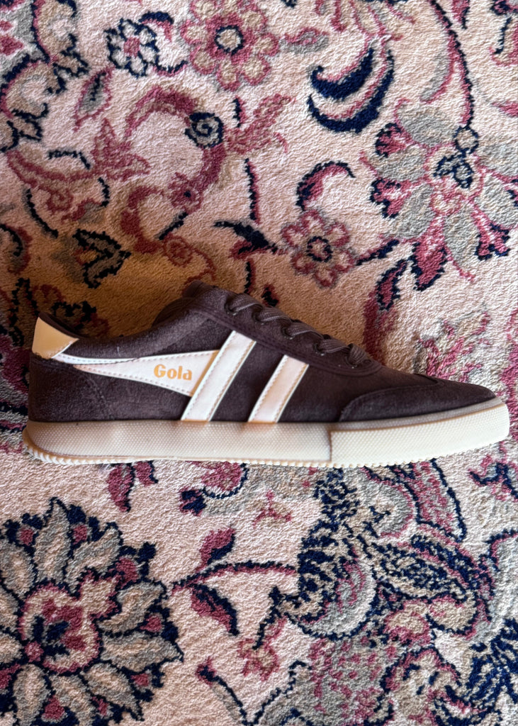 Brown sneaker with white sole on a patterned carpet