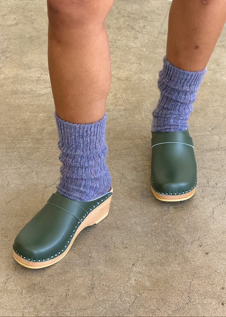 Green clogs worn with purple socks on a concrete floor