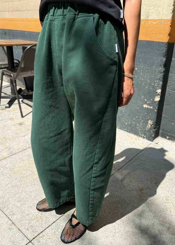 Person wearing green pants standing on a sidewalk with a blurred background