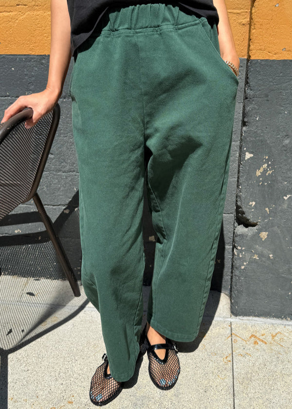Person wearing green pants and black shoes on a sidewalk.