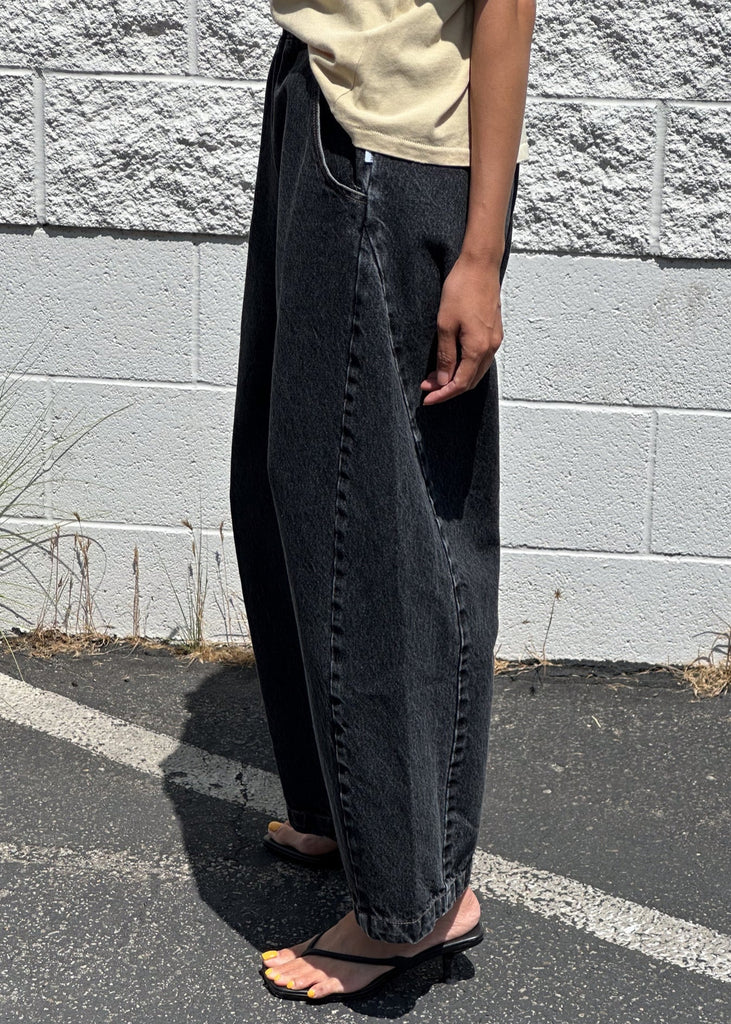 Person wearing black jeans and a beige shirt against a gray concrete wall.