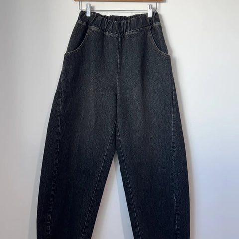 Black jeans hanging on a wooden hanger against a white background