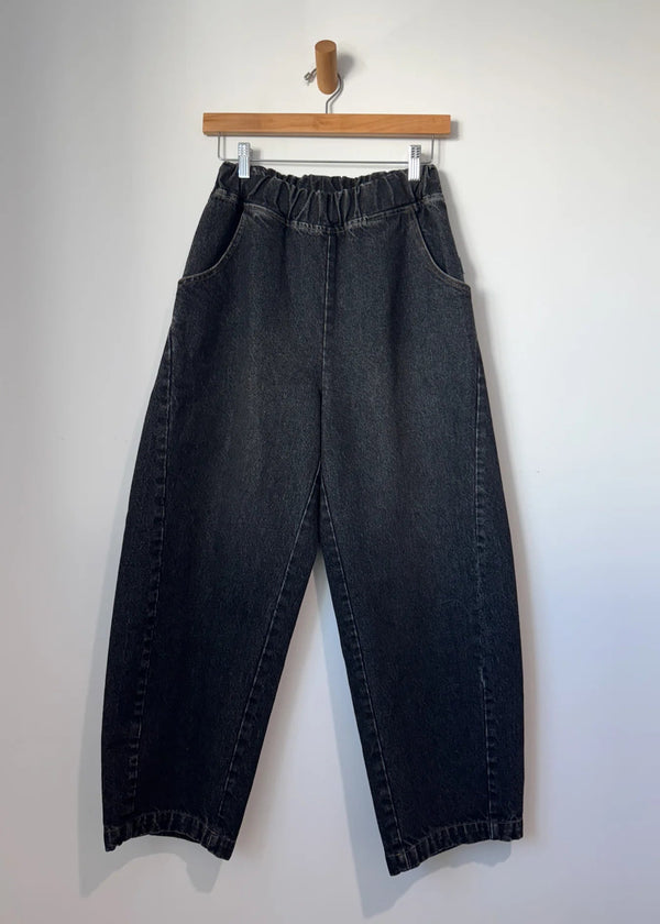 Black jeans hanging on a wooden hanger against a white background