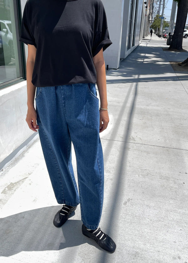 Person wearing a black shirt and blue jeans standing on a sidewalk.