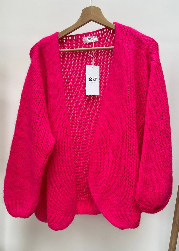Pink knitted cardigan on a hanger with a visible brand tag against a white background
