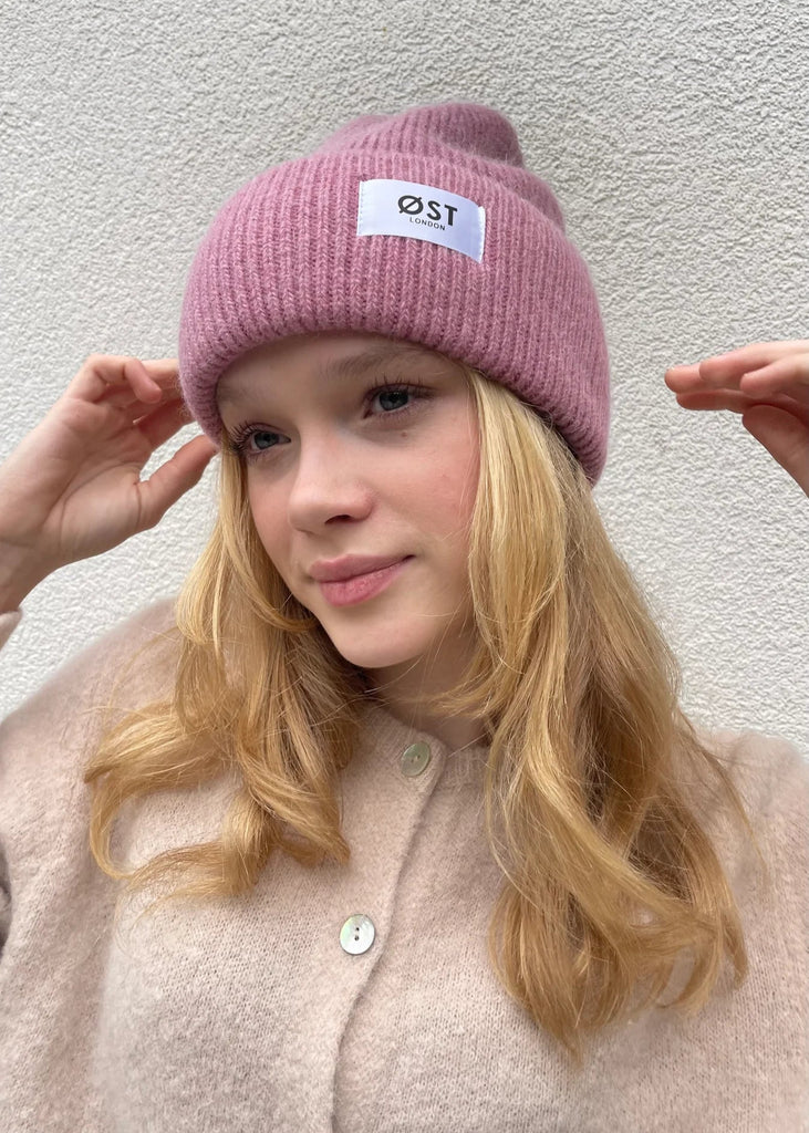 Person wearing a pink beanie with a logo against a plain background