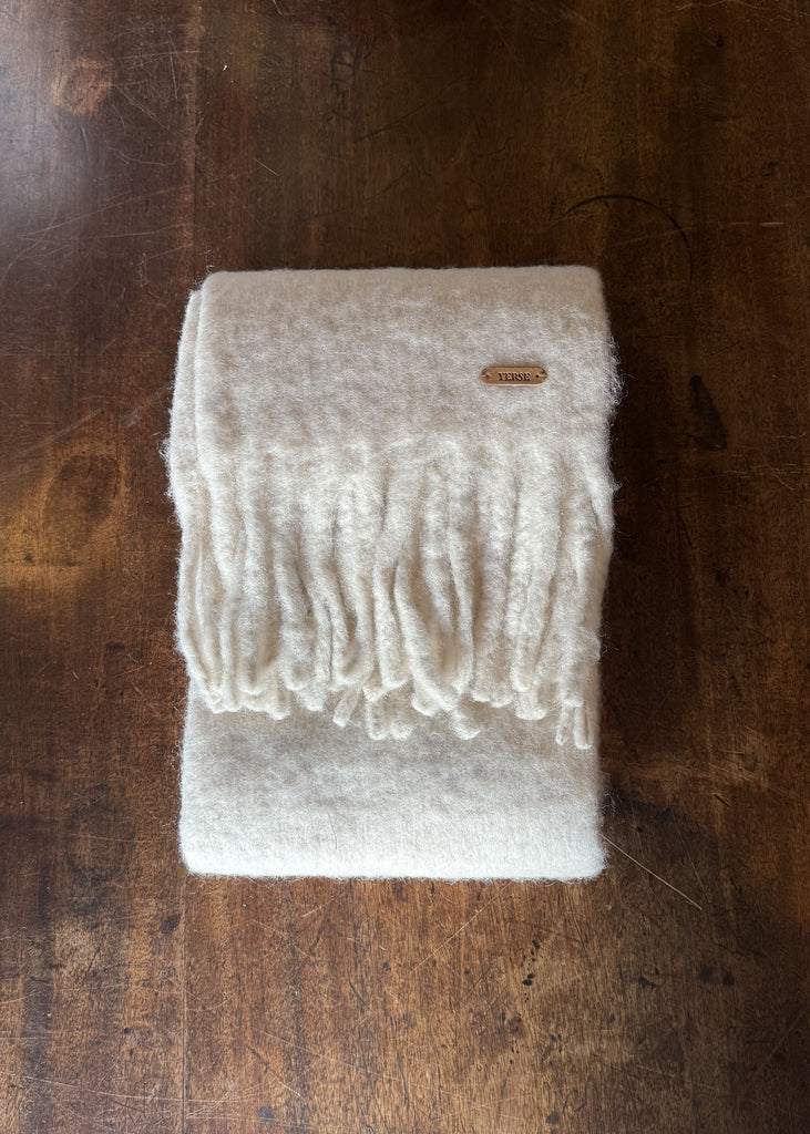 White knitted blanket with fringes on a wooden surface