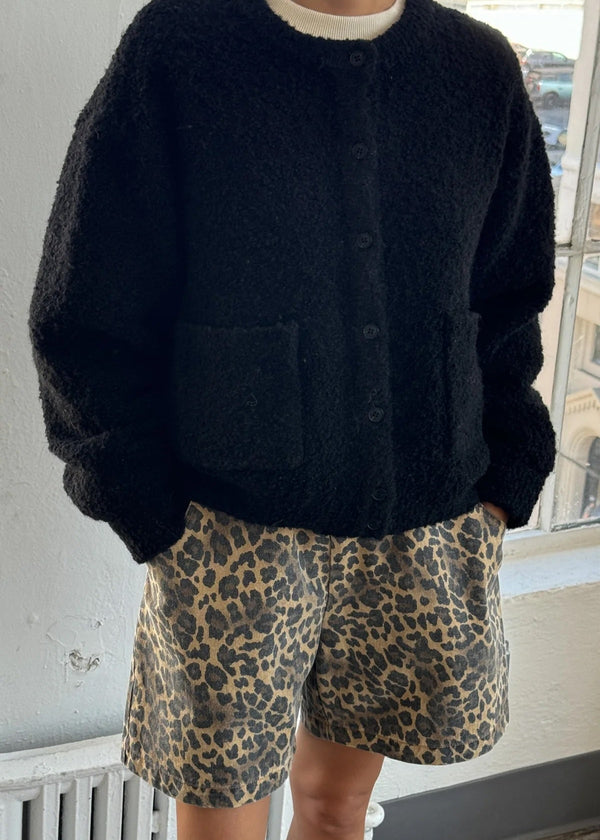 Person wearing a black cardigan and leopard print shorts indoors.