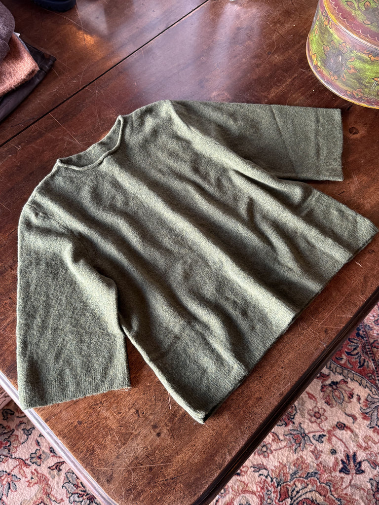 Green sweater on a wooden surface with a patterned rug underneath