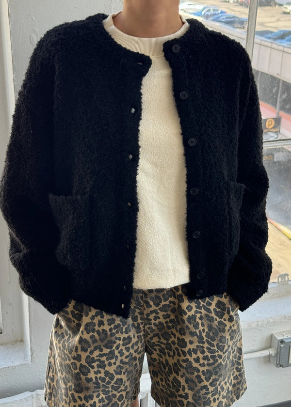 Person wearing a black cardigan, cream shirt, and leopard print shorts indoors.