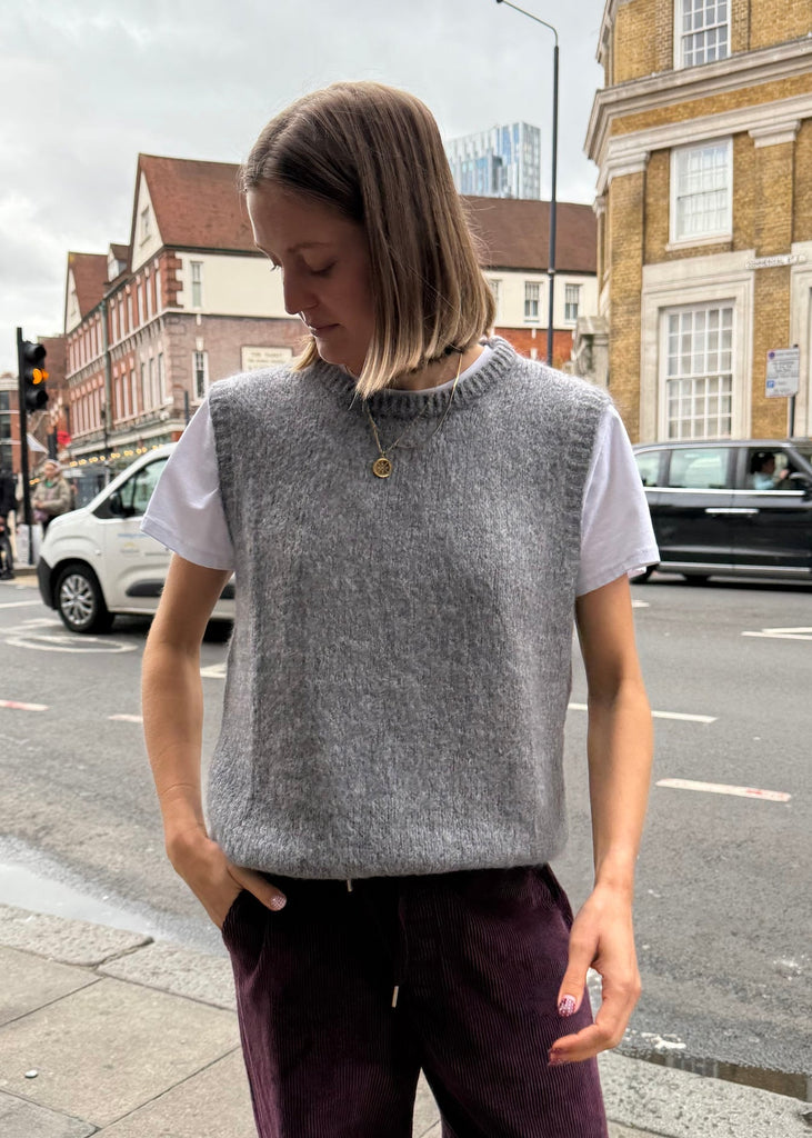 Person wearing a gray sleeveless sweater on a city street