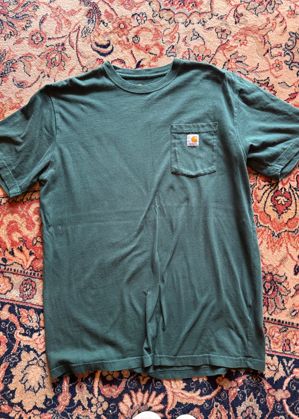 Green t-shirt with a brand logo on a patterned rug