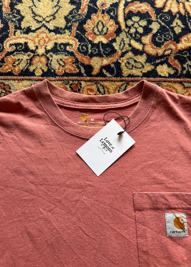 Pink t-shirt with a brand logo on a patterned rug