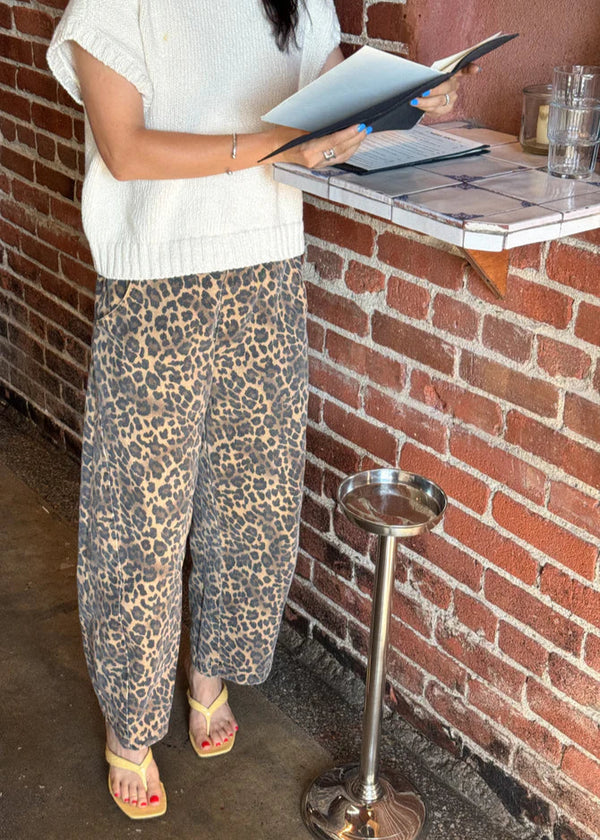 Person wearing leopard print pants and a white top, standing near a brick wall.